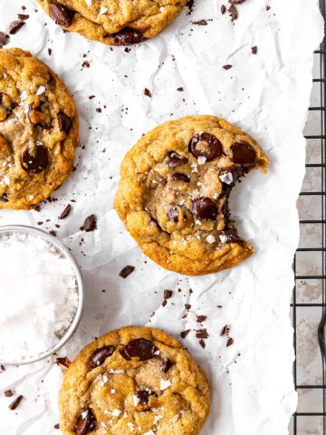 Banana chocolate chip cookie with a bite taken out of it and a cup of flaky salt.