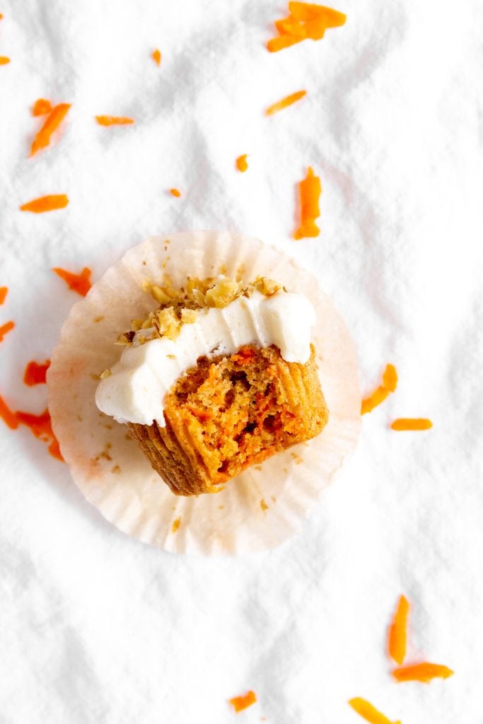 Vegan carrot cake cupcake with a bite taken out of it sitting on its wrapper.