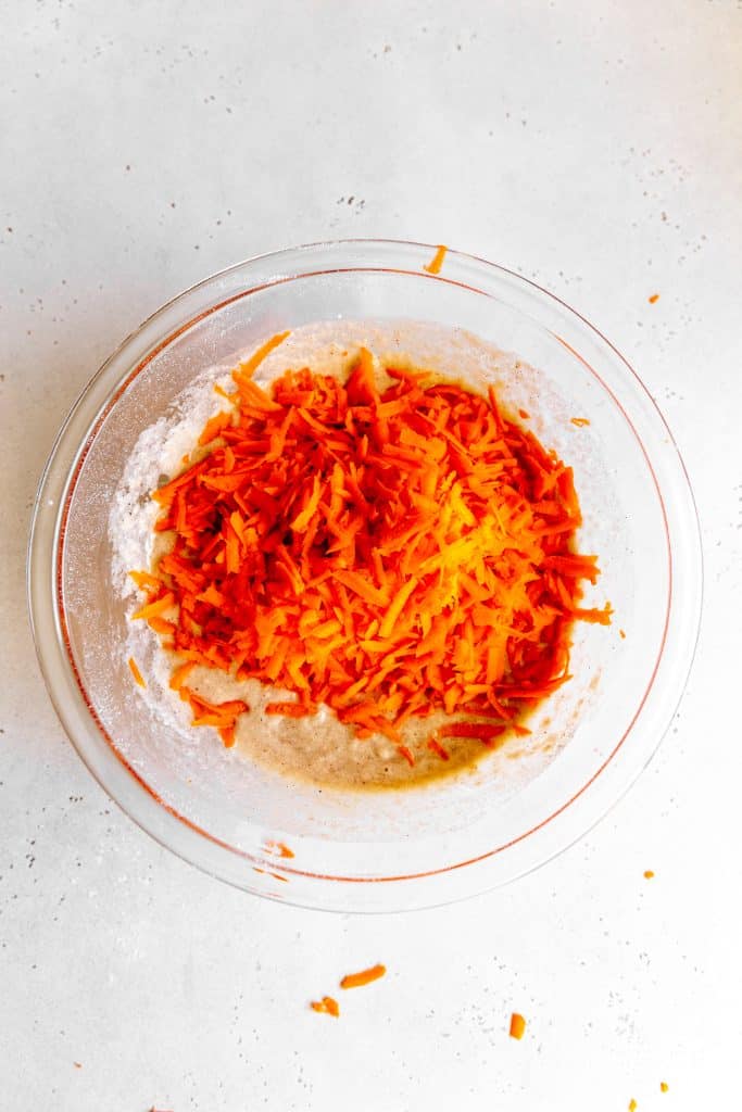 Glass bowl of cake batter topped with grated carrots.