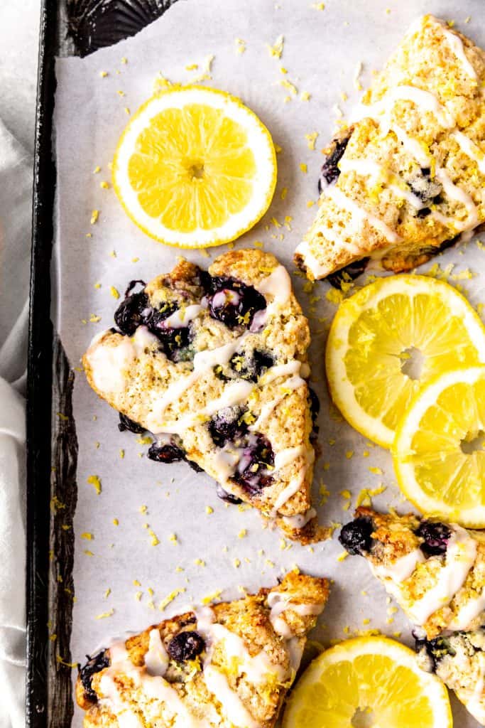 Lemon blueberry scones on a baking sheet with lemon slices and a linen napkin.