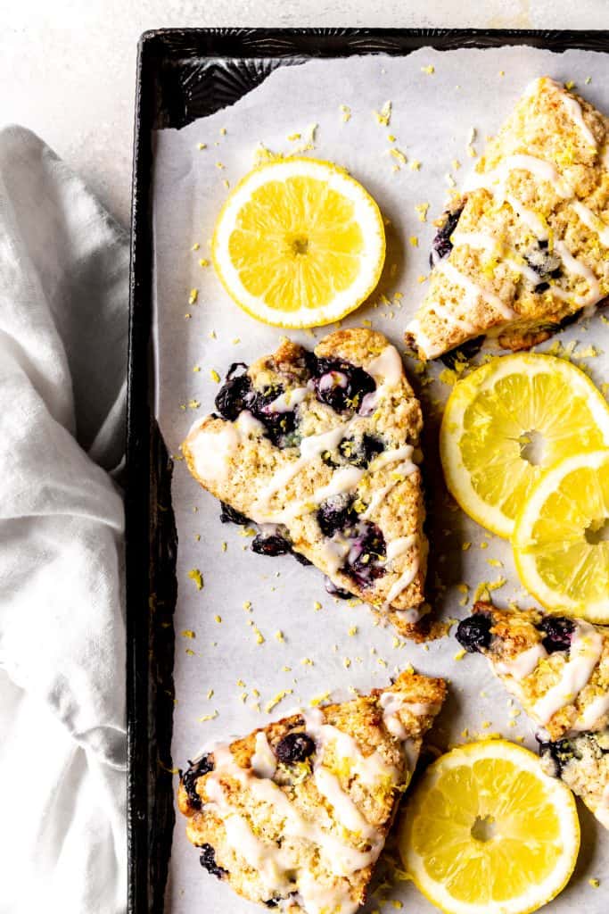 Lemon blueberry scones on a baking sheet with lemon slices and a linen napkin.