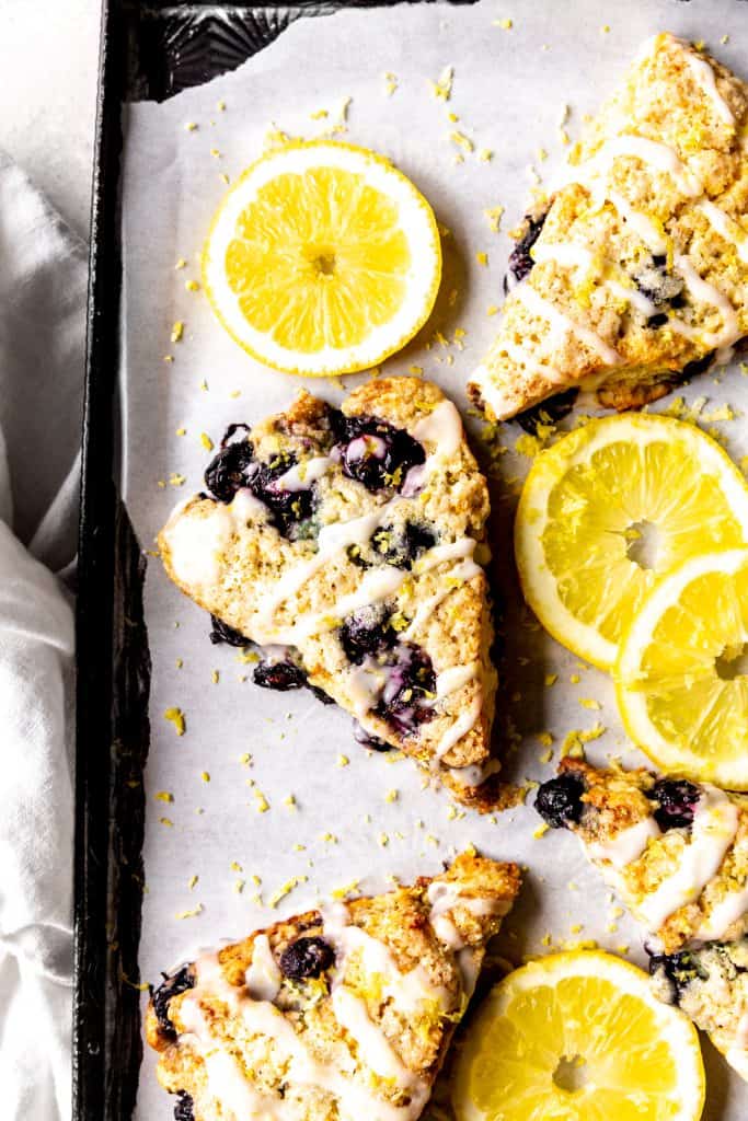 Lemon blueberry scones on a baking sheet with lemon slices and a linen napkin.