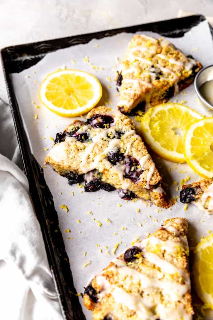 Lemon blueberry scone on a baking sheet with lemon slices and blueberries.