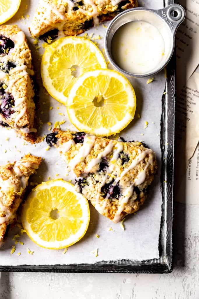 Lemon blueberry scone on a baking sheet with lemon slices.