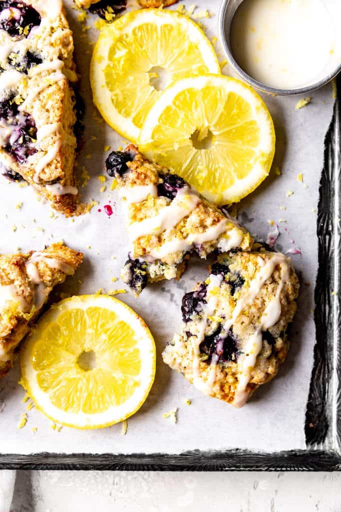 Lemon blueberry scone broken in half on a baking sheet with lemon slices.