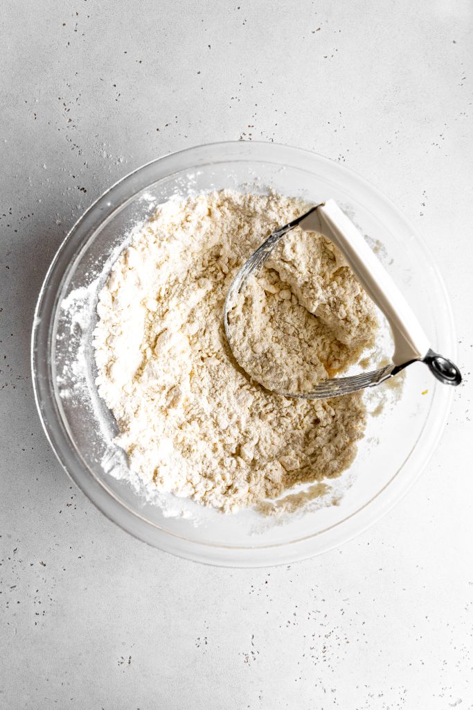 Pastry cutter in a glass bowl of dry ingredients for scones.