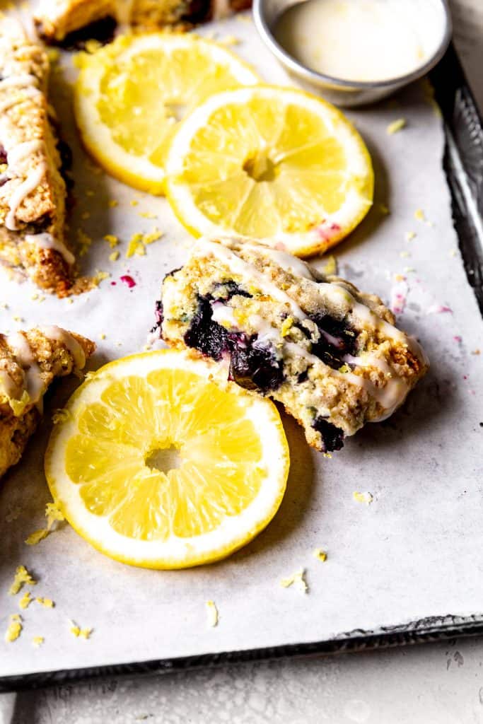 Half of a lemon blueberry scone propped on a lemon slice on a baking sheet.