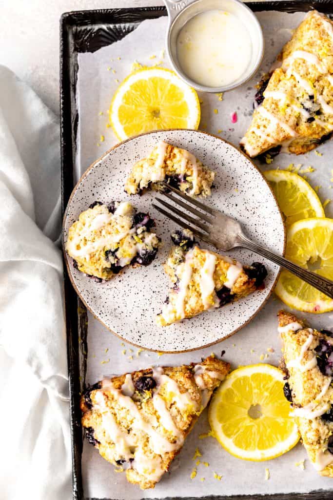 Lemon blueberry scone broken in pieces on a white plate with a fork.