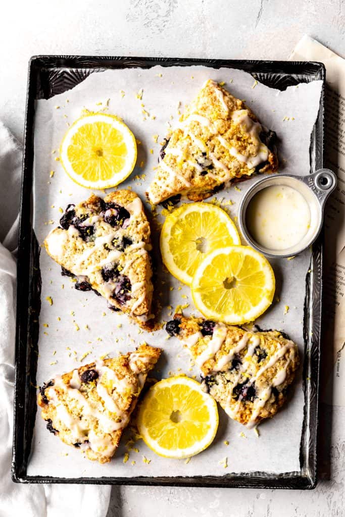 Lemon blueberry scones on a baking sheet with a cup of lemon glaze.