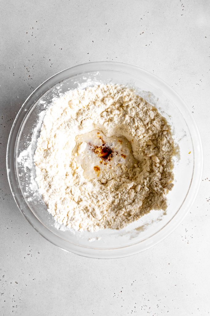 Milk and vanilla extract in a well of dry ingredients in a glass bowl.