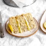 Slice of lemon poppyseed cake on a plate in front of the whole cake.