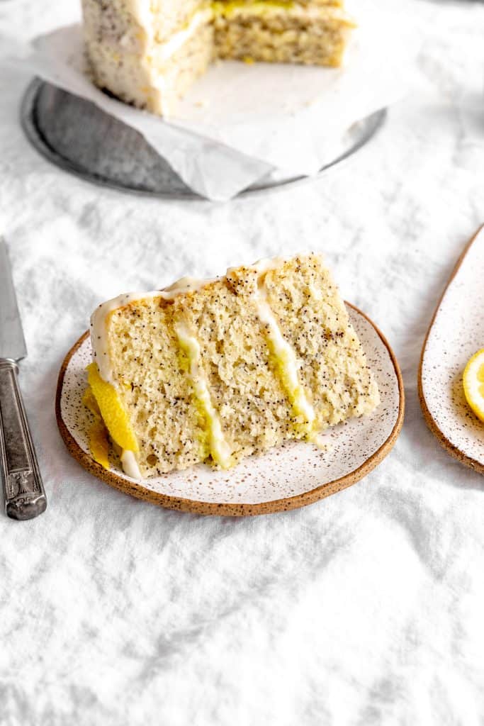 Slice of lemon poppyseed cake on a plate in front of the whole cake.