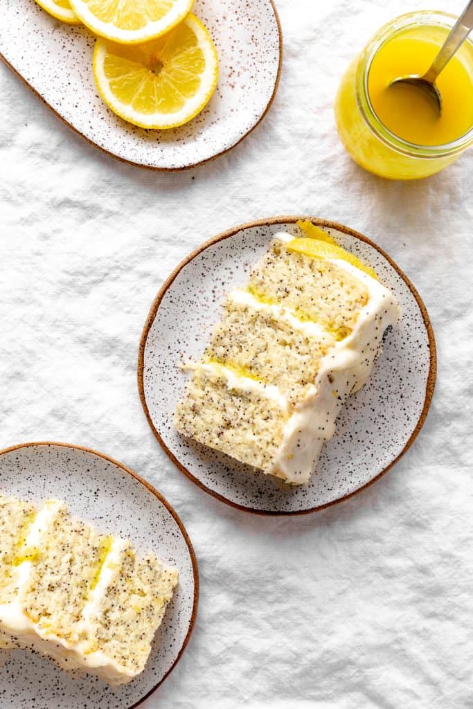 Slice of lemon poppyseed layer cake, lemon slices and a jar of lemon curd.