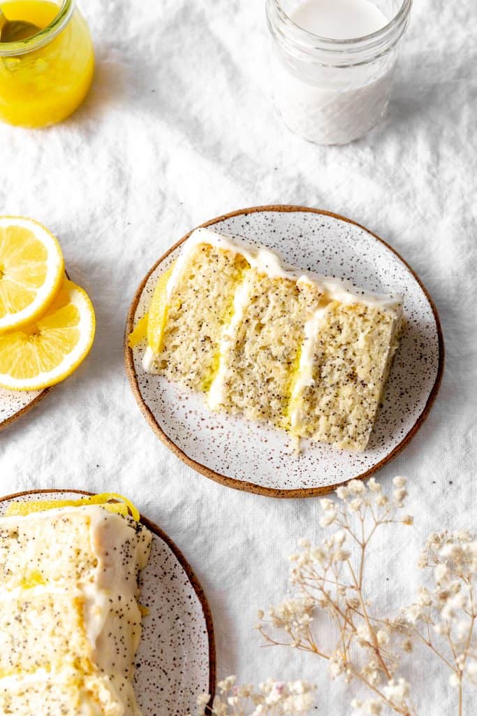 Slice of lemon poppyseed layer cake, a glass of milk and fresh lemon slices.