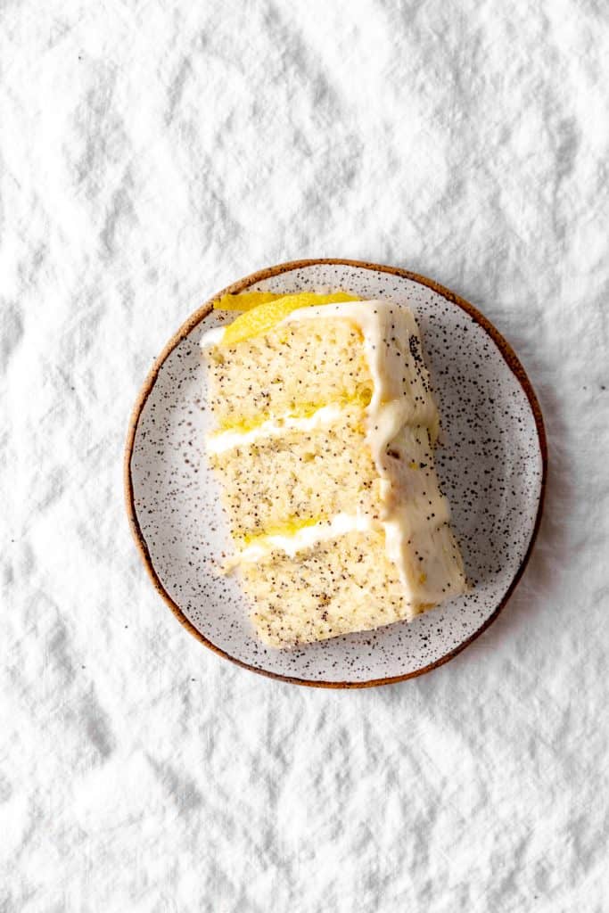 Slice of lemon poppyseed layer cake on a white plate.