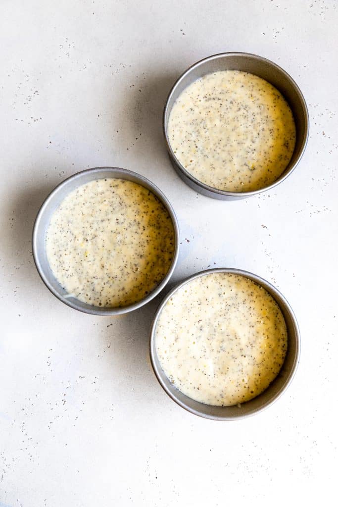 Three round cake pans filled with lemon poppyseed cake batter.