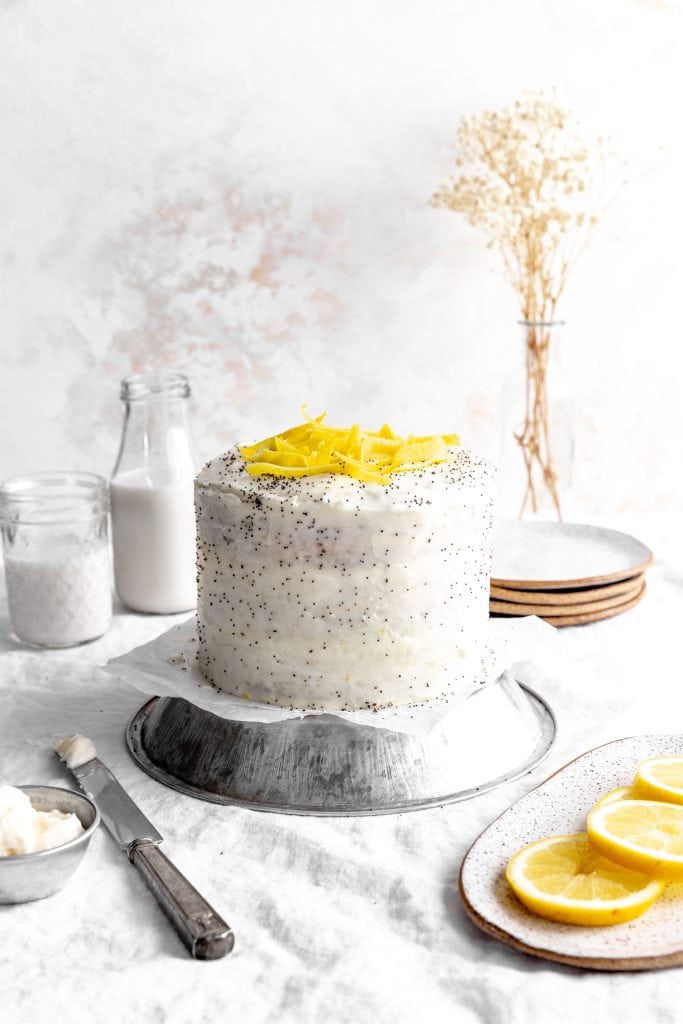 Lemon poppyseed layer cake and fresh lemon slices in front of a jug of milk.