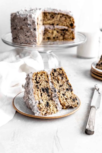 Slice of Oreo cake on a plate next to a knife covered in frosting.