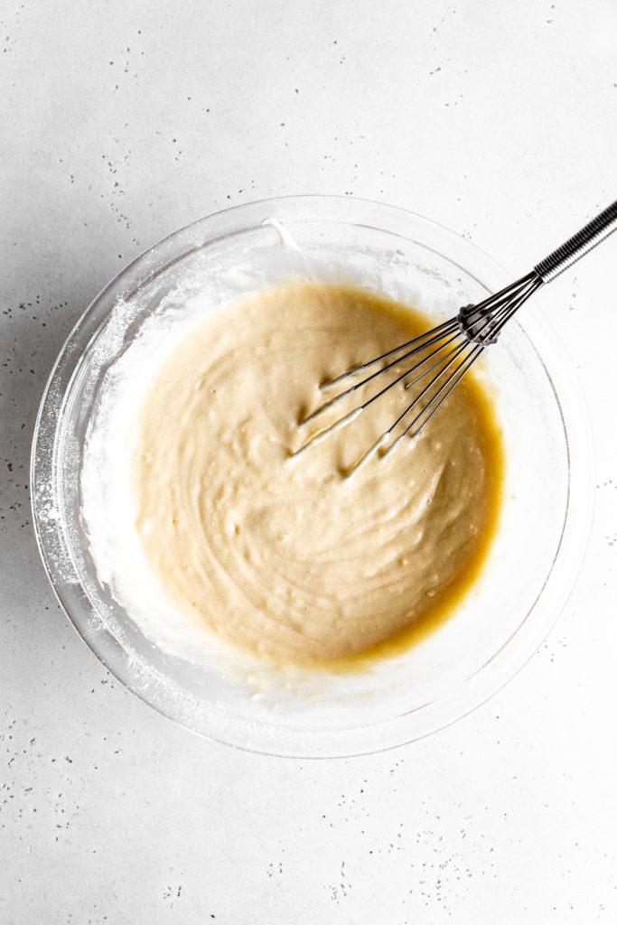 Glass bowl filled with vanilla cake batter and a wire whisk.