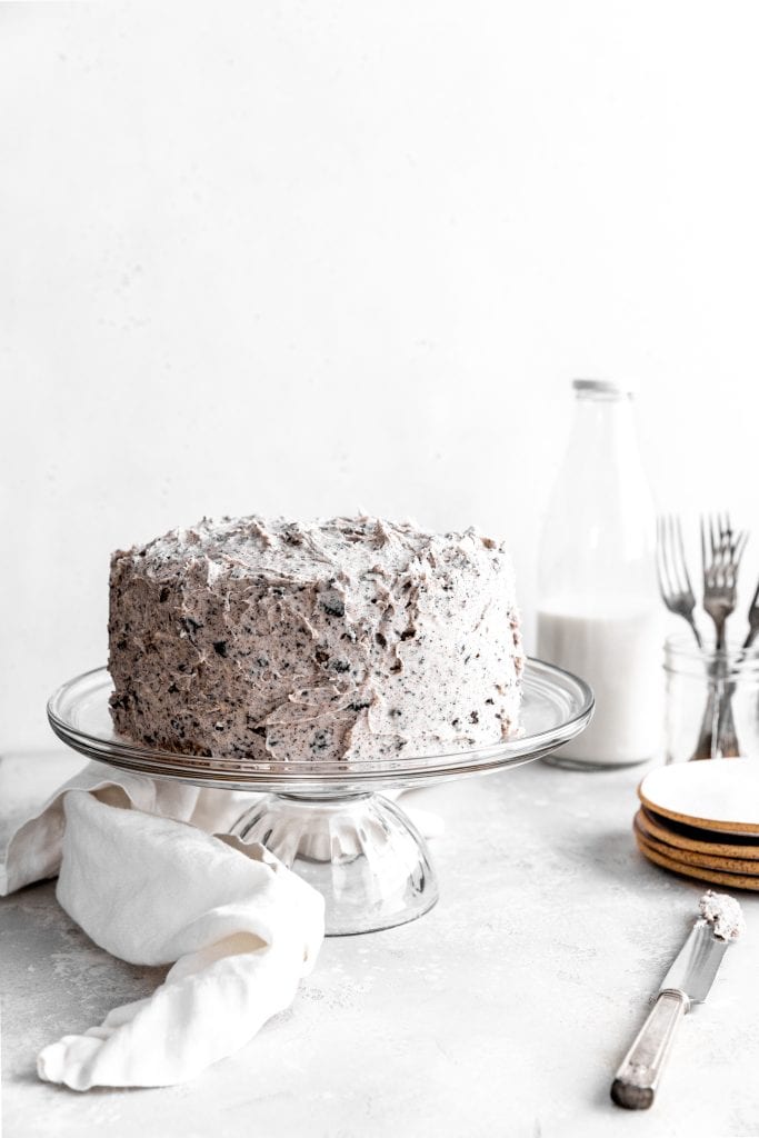 Oreo cake on a glass cake stand in front of a jug of milk.