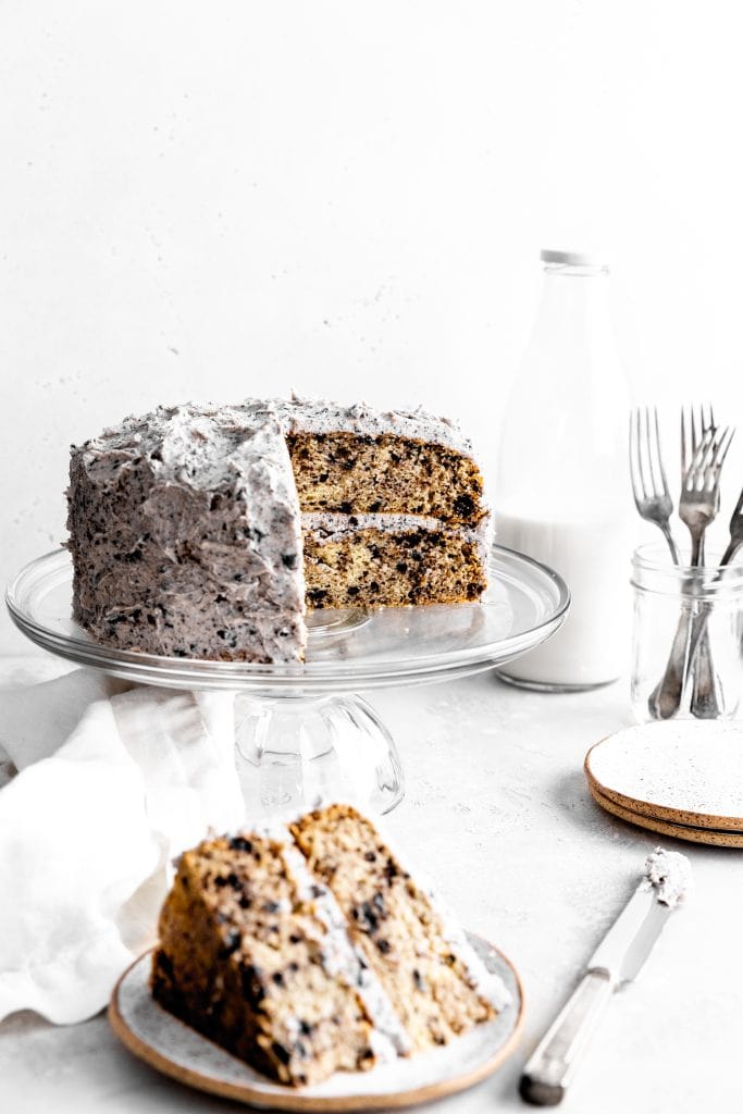 Oreo cake with slices missing on a glass cake stand in front of a jug of milk.