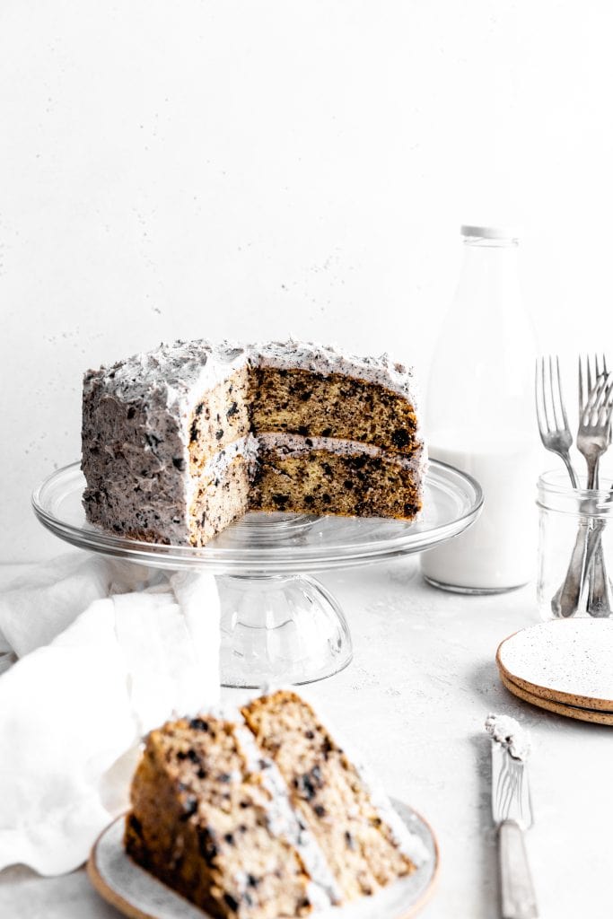 Oreo cake with slices missing on a glass cake stand in front of a jug of milk.