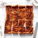 Snickerdoodle bars arranged on a white surface with a knife and a glass of milk.