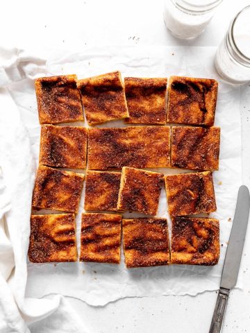 Snickerdoodle bars arranged on a white surface with a knife and a glass of milk.