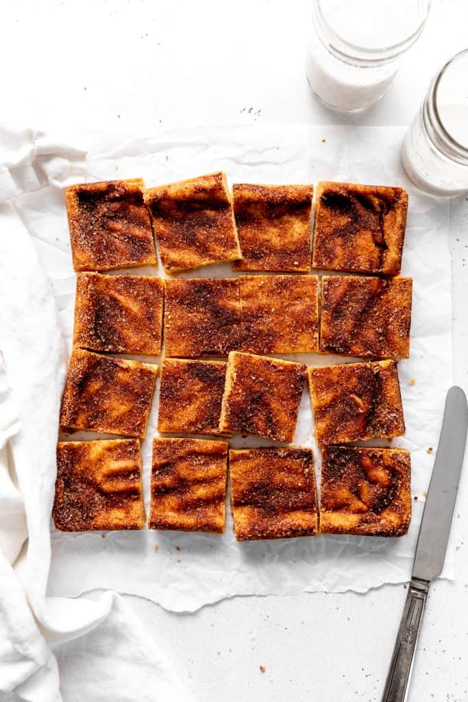 Snickerdoodle bars arranged on a white surface with a knife and a glass of milk.