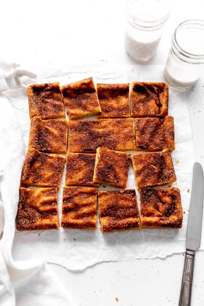 Sliced snickerdoodle bars, a knife and two glasses of milk.