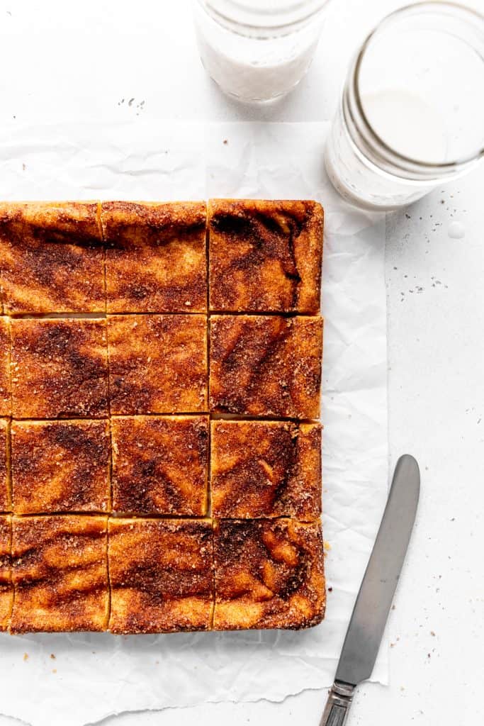 Snickerdoodle bars arranged in a square, a knife and a glass of milk.