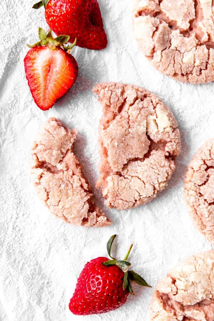 Broken in half strawberry crinkle cookie and sliced strawberries.