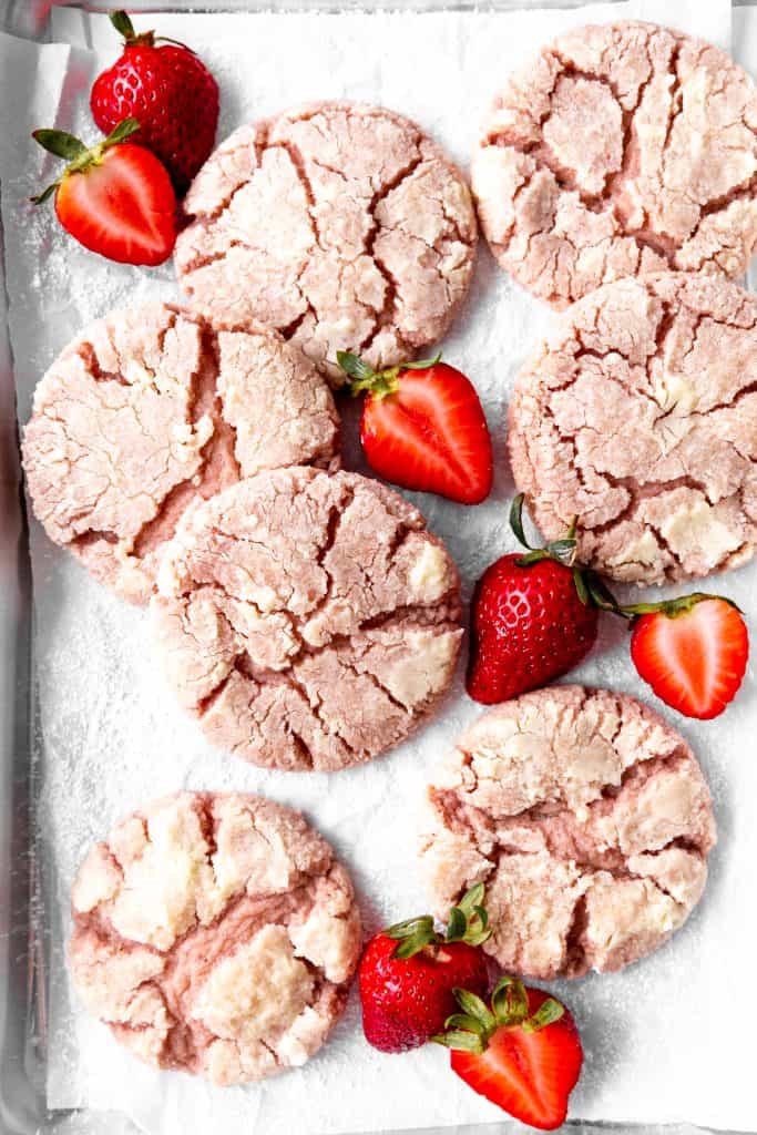 Strawberries crinkle cookies on a baking sheet scattered with strawberries.