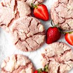 Strawberry crinkle cookies on a white surface with sliced strawberries.