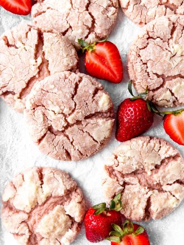 Strawberry crinkle cookies on a white surface with sliced strawberries.