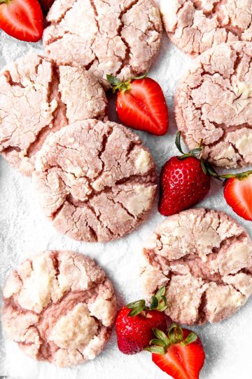Strawberry crinkle cookies on a white surface with sliced strawberries.