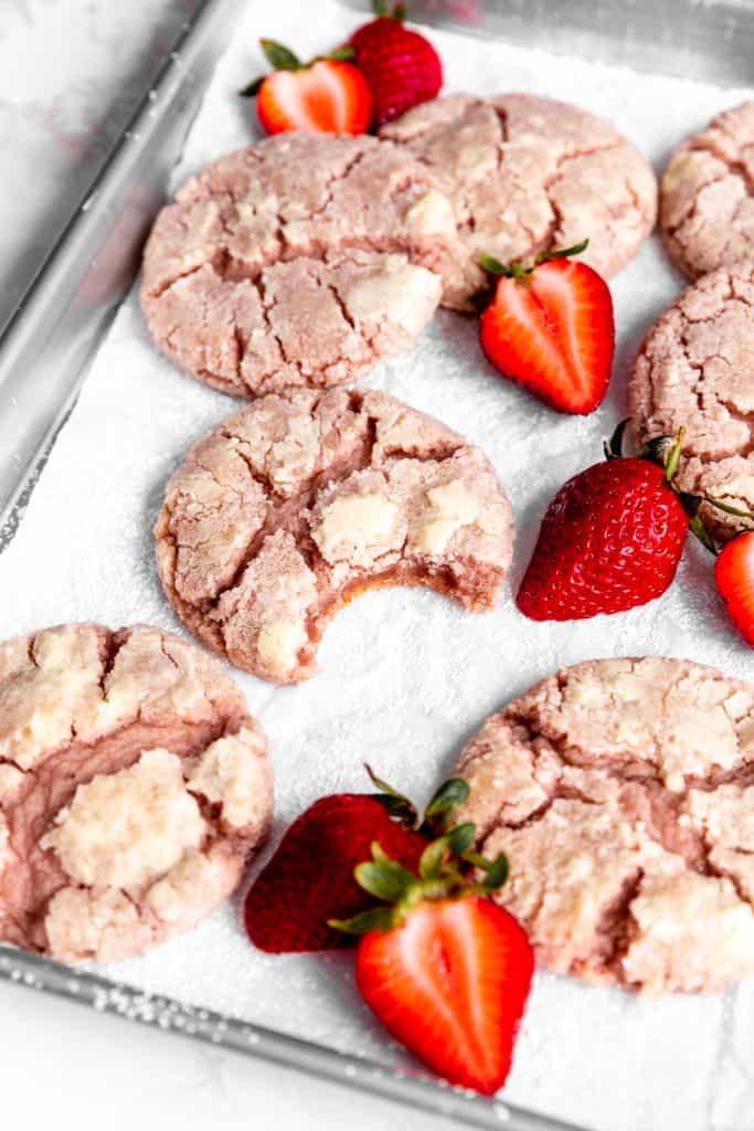 Strawberry crinkle cookie with a bite taken out of it on a baking sheet with more cookies.