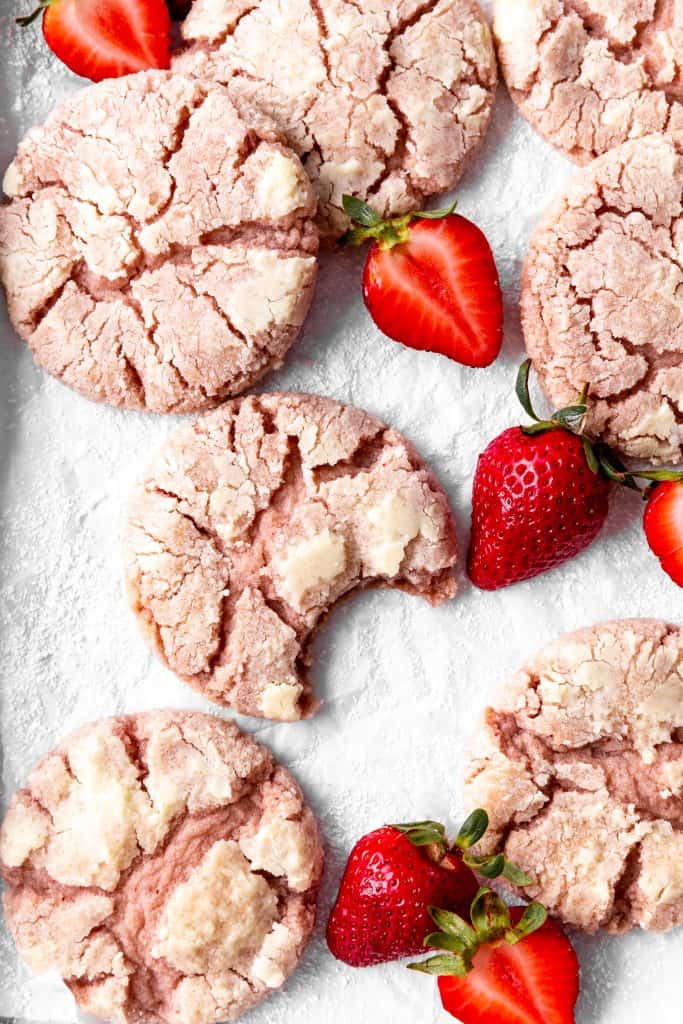 Strawberry crinkle cookie with a bite taken out of it on a baking sheet with more cookies.