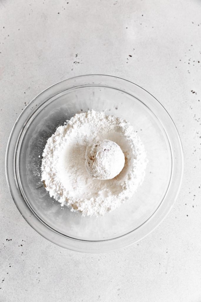 Strawberry cookie dough being rolled in powdered sugar.