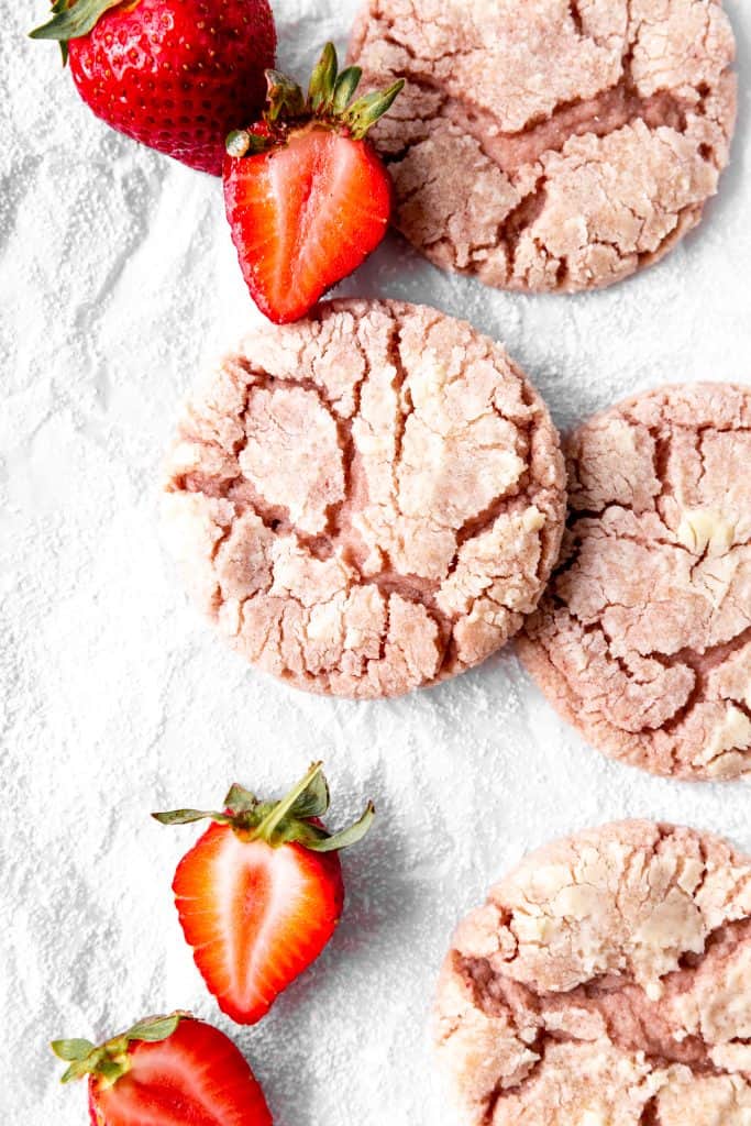 Strawberry crinkle cookies on parchment paper with sliced strawberries.