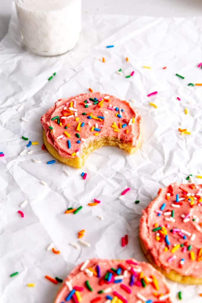 Frosted sugar cookie with a bite taken out of it in front of a glass of milk.