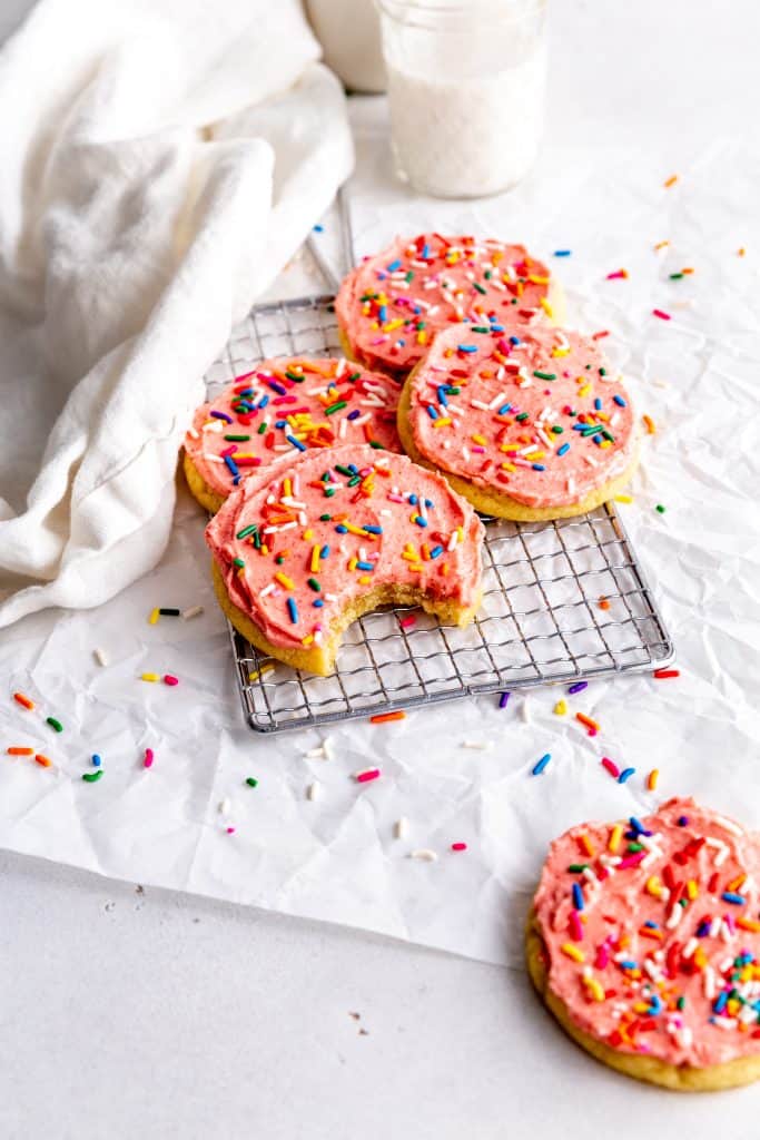 Frosted vegan sugar cookies on a wire cooling rack and a glass of milk.