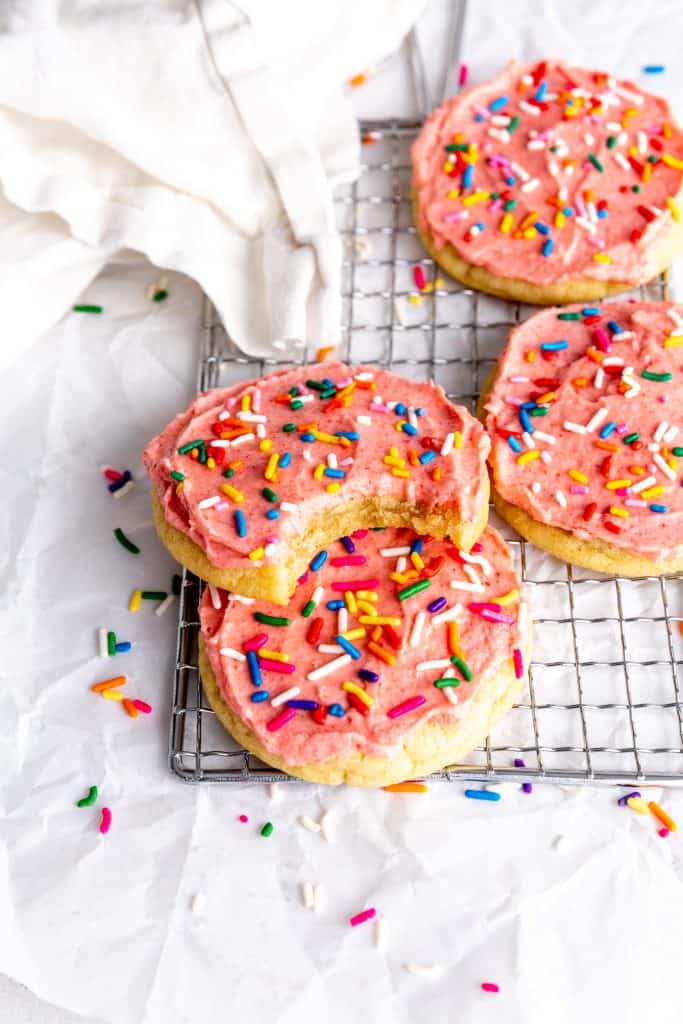 Vegan frosted sugar cookie with a bite taken out of it stacked on another cookie on a cooling rack.