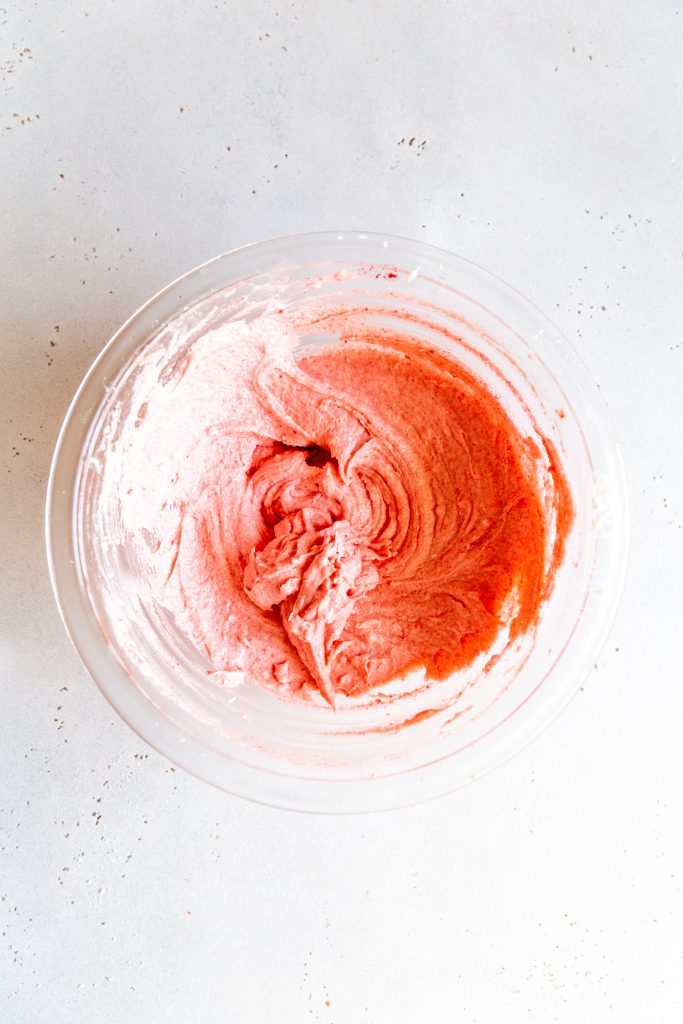 Glass bowl filled with strawberry frosting.