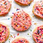 Pink frosted sugar cookies on a white background scattered in sprinkles.