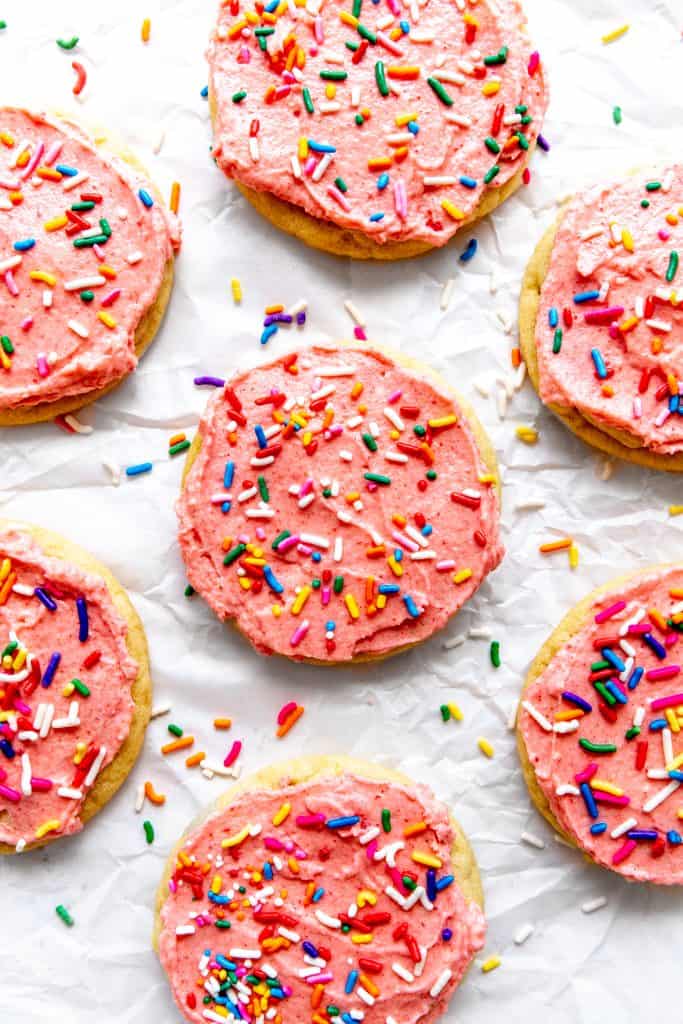 Pink frosted sugar cookies on a white background scattered in sprinkles.