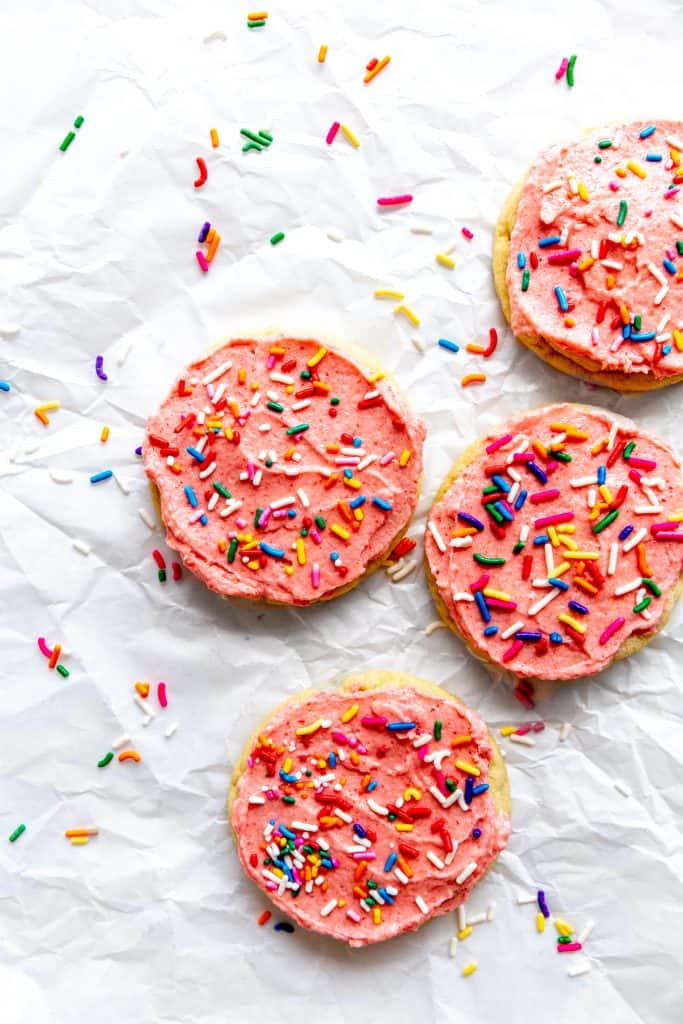 Pink frosted sugar cookies on a white background scattered in sprinkles.