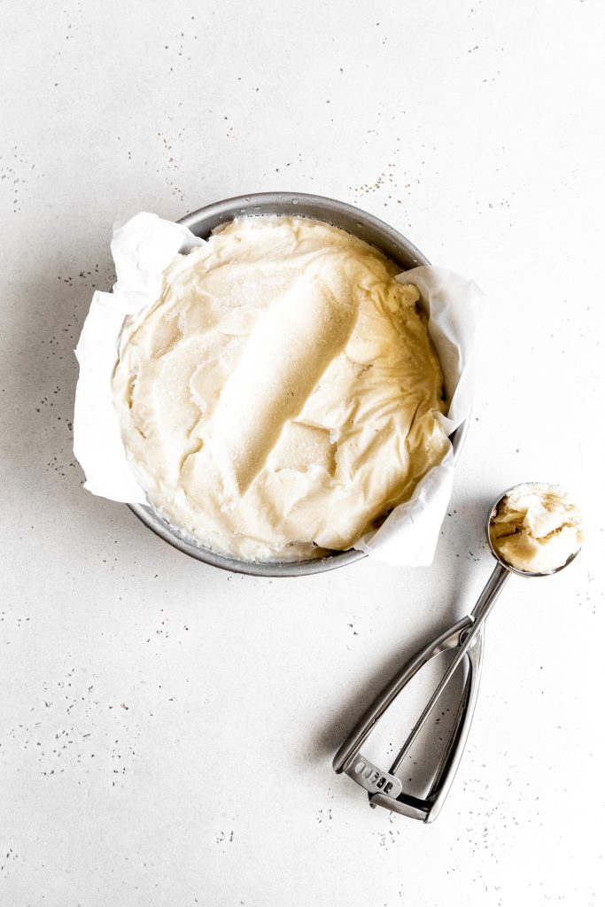 Round cake pan of vanilla ice cream and an ice cream scoop filled with ice cream.