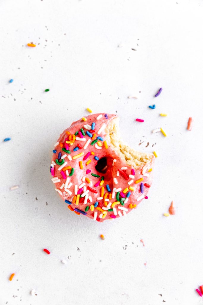 Baked donut with pink icing and sprinkles with a bite taken out of it.