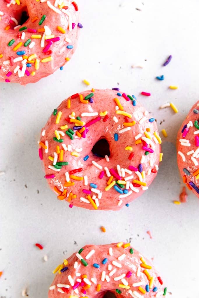 Frosted baked donut on a white surface covered in sprinkles.